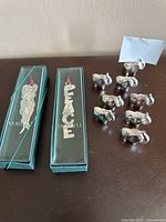 Metal elephant place card holders in front of a wall, along with two boxed Christmas decorations.