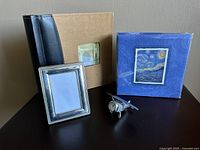 Set of four items including two photo albums, silver-plated frame, and airplane figurine with clock displayed on table.