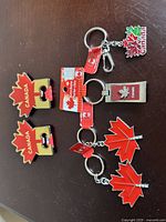 Five Canadian motif metal keychains and bottle openers on dark surface, featuring maple leaves and 'Canada' text, red, silver, and green colors