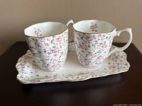 Two Royal Albert Rose Confetti pattern mugs on a matching rectangular tray, showing floral design and gold trim.