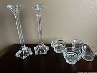 Photo shows set of 2 tall crystal candle holders with octagonal bases and floral tops alongside 4 smaller glass candle holders with octagonal bases.