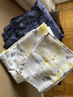 Two folded tablecloths and a set of four yellow placemats on a chair showing colors and patterns