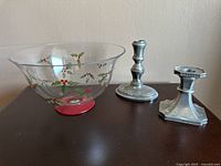 Photo showing the two pewter candle holders alongside the glass bowl with holly design and red base on a dark surface.