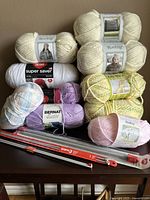 Yarn skeins stacked on a table with knitting needles laid in front.