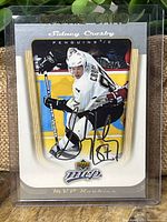 Front view of 2005 Upper Deck MVP Sidney Crosby rookie hockey card number 87 showing player in white Penguins jersey in protective hard plastic case. Features silver facsimile autograph on front and gold-white border.