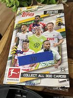 Front view of sealed 2021-22 Topps Bundesliga hobby box featuring multiple Bundesliga players and branding, showing pack count and promotional details.