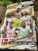 Front of closed shrink-wrapped box featuring Bundesliga players, Topps branding, and collect all 300 cards note.