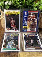 Four Michael Jordan basketball cards from Topps, Fleer, and Hoops in protective sleeves with background plant decor.