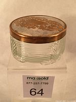 Front side view of the footed vintage vanity jar showing clear ribbed opaque glass base with molded feet and metal lid with visible patina wear.