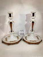Front view of the pair of white porcelain candlesticks with gold trim and floral decals on a flat surface.
