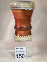 Front view of the chalice showing the matte brown exterior with light blue drip near the rim, set on clear stand with lot number 150.