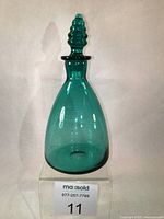 Front view of hand blown teal green glass decanter with pointed bee hive style stopper, showcasing the shape and color.