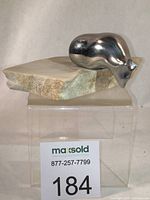 Abstract silver-toned aluminum polar bear sculpture mounted on a natural stone slab base, shown from front angle on a clear display stand with lot number.