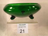 Front angle view of green hand blown glass bowl showing rounded shape and snail scroll feet.