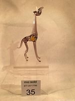 Glass giraffe figurine displayed on clear stand showing full front and left profile.