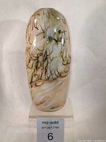Front angled view of the hand blown Murano style bud vase showing the marbleized multiple brown shades on cream and clear glass, oval elongated form with small opening.