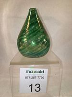 Front view of small hand blown glass bud vase, green and white spirals, teardrop shape, on clear cube stand.