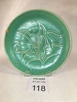 Front view of a green ceramic plate with incised tulip floral design and visible chips and cracks.
