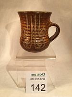 Front view of the Ted Diakow stoneware mug showing wax resist pattern on brown glaze.