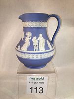 Front side view of blue Wedgwood Jasperware pitcher showing white relief figures and decorative bands.