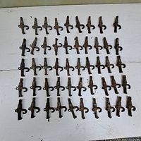 Overview of 49 antique metal maple syrup spiles arranged in rows on a white surface, showing varying patinas and wear.