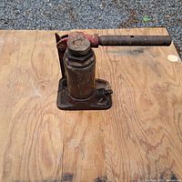 Two images showing two hydraulic bottle jacks separated on plywood surface, both rusted with red hydraulic handles attached.