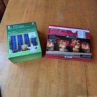 Two boxes of decorative lights on wooden surface: green box for clear curtain star reflector lights, red box for Sylvania LED microdot lights