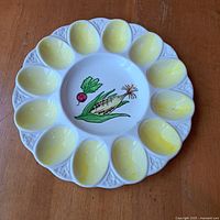 Top view of devilled egg platter showing all 12 yellow egg-shaped indentations and vegetable illustration at center