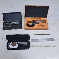 Complete set of three micrometers, two metal rulers, and one metal scribe, displayed on a white surface