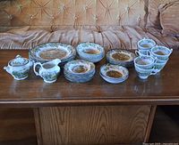 Full dish set laid out on wooden table showing stacks of plates, bowls, cups, creamer, and sugar bowl.