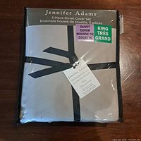 Front view of packaged Jennifer Adams king size 3-piece duvet cover set folded and tied with black ribbon in plastic zippered case.