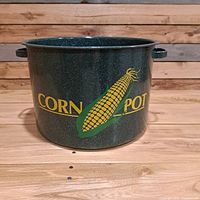 Front view of green speckled enamelware corn pot with yellow corn cob graphic and lettering