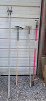 Full view of four gardening tools leaning against a wall in gravel area.