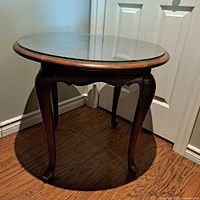 Front angle view of round coffee table showing wooden curved legs and circular glass top.