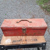 Closed view of red metal toolbox 19" long with metal handle and latch. Visible wear and rust.