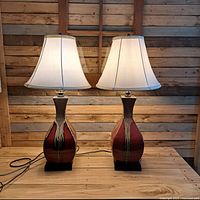 Pair of mid century drip glazed ceramic table lamps with white fabric shades on a wooden table against wood paneled wall.