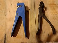 Blue-handled hand tool and black cutting pliers placed on wooden surface