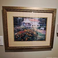 Framed picture of a white house with a colorful flower garden in front, hung on a wall.