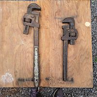 Photo showing both pipe wrenches side by side on a wooden surface, highlighting size difference and condition.