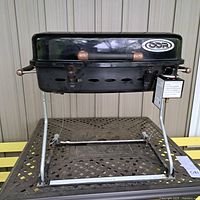 Front view of the black DDR portable propane BBQ grill with foldable legs and attached burner control.