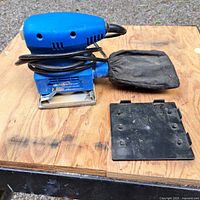 Blue Powerfist Dustless 1/4 sheet palm sander with black dust bag and detachable sanding pad on wooden surface