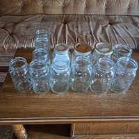 Front view of 13 various size preserving jars arranged on table in front of couch showing different designs and lid types including 5 Atlas jars.