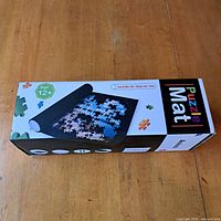 Box packaging showing the puzzle mat rolled with puzzle pieces on top, age recommendation 12+ and product name Puzzle Mat