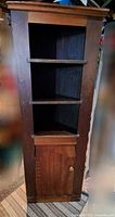 Front view of wooden corner cupboard showing three shelves and bottom door area.