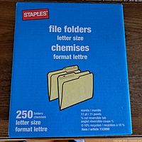 Photo of closed Staples file folder box showing product details including 250 count, letter size, 10% recycled content, reversible tab.