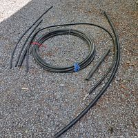 Roll of black 1/2 inch PE Leger Utility Pipe both coiled and several cut pipe pieces laid on gravel.