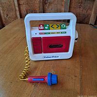 Frontal view of Fisher Price cassette player with microphone attached on wooden surface
