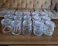 Set of 15 vintage glass preserving jars with metal clip lids and rubber sealing rings arranged on a wooden surface.