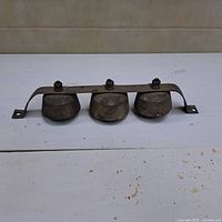 Front view of three solid brass shop keeper's bells mounted on iron bracket showing aged patina.