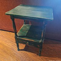 Side view of the vintage wooden side table showing square top, turned legs, lower open shelf, and single drawer closed.